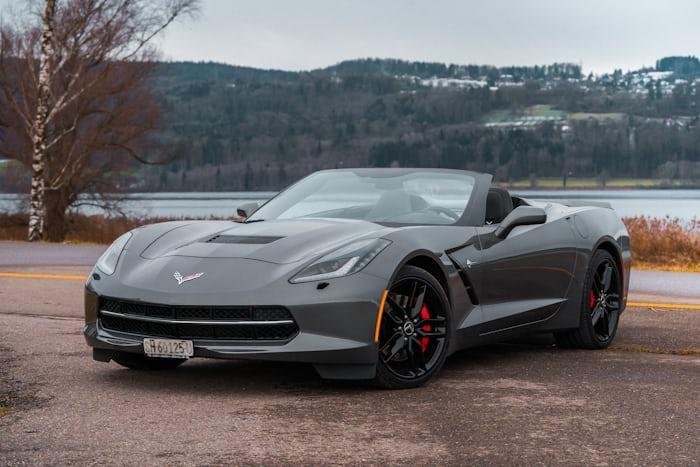Gray Chevrolet Corvette with red brakes parked on a road near a lake.