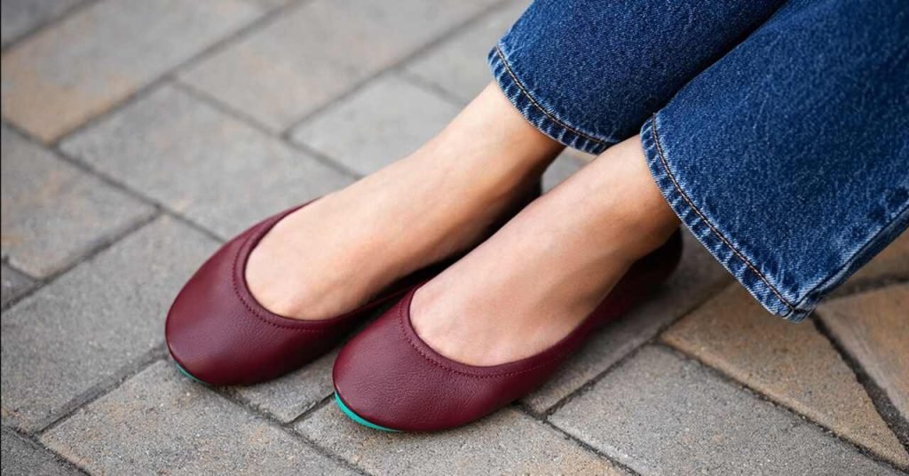 Burgundy Tieks flats styled with jeans on a stone walkway.