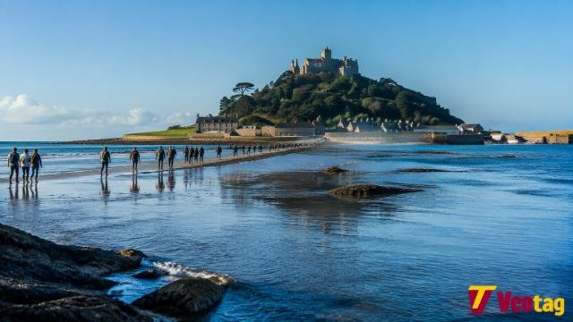 St Michael’s Mount Cornwall castle with tidal causeway and visitors walking across wet sand