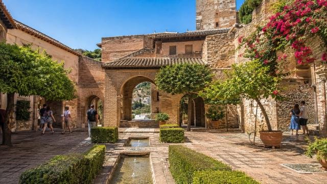 Alcazaba of Málaga Moorish courtyard with stone arches, fountains, orange trees, and bougainvillea in soft morning light.