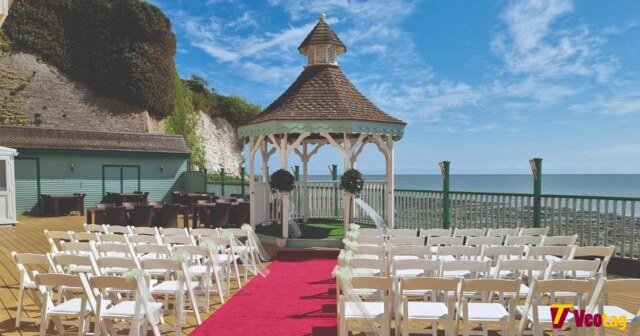 Outdoor seaside wedding ceremony setup with white chairs, red carpet aisle, and elegant gazebo overlooking the ocean.