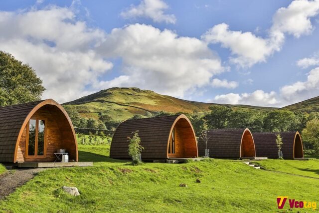 Wooden glamping pods at The Quiet Site in the Lake District, England, surrounded by green hills and scenic countryside.