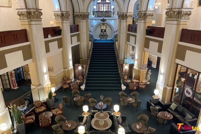 Interior view of The Grand Scarborough hotel lobby featuring a grand staircase, ornate columns, elegant seating areas, and classic architecture.